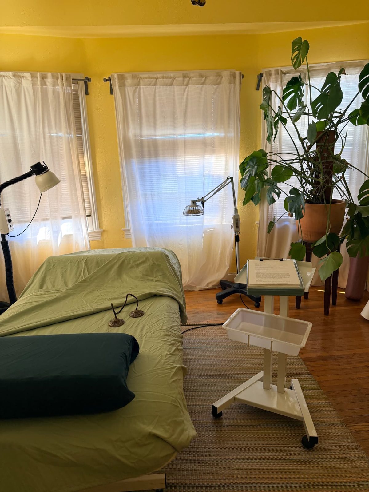 Treatment table dressed in soft green linen beside sunlit curtained windows