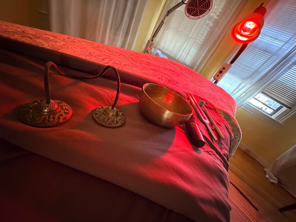 A singing bowl, tingsha chimes, and tuning forks resting on the table under warm light